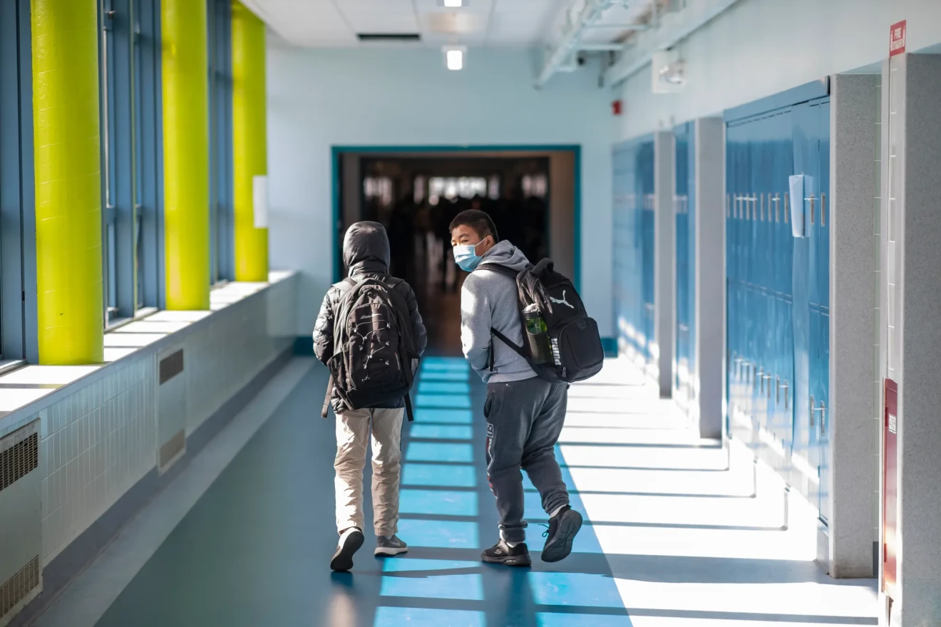 Two student walk down a hallway wearing backpacks.
